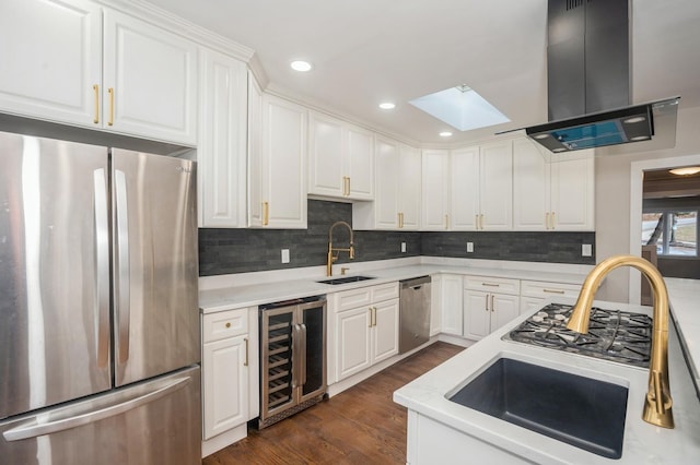 kitchen with beverage cooler, appliances with stainless steel finishes, a skylight, island exhaust hood, and a sink