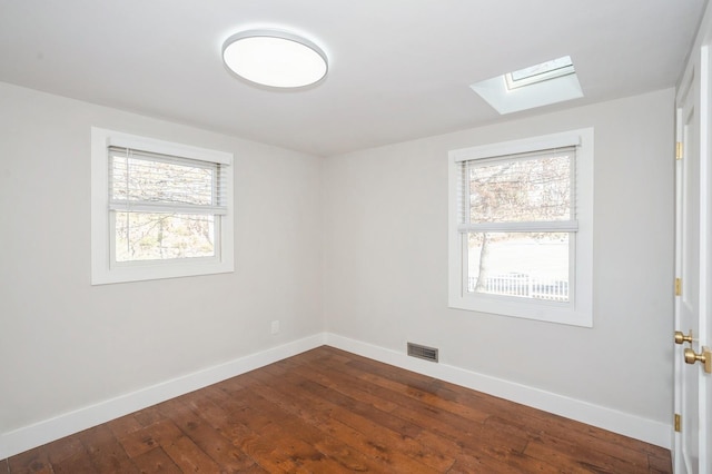 spare room featuring dark wood-style floors, a skylight, baseboards, and visible vents