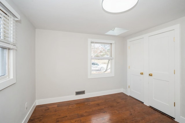 unfurnished bedroom featuring visible vents, a skylight, baseboards, and wood-type flooring