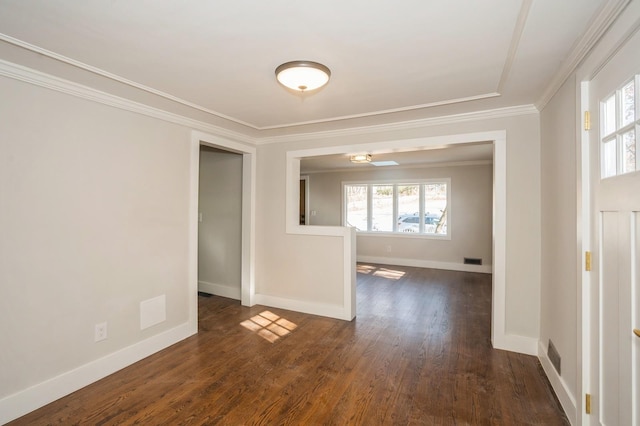 spare room featuring dark wood-type flooring, visible vents, baseboards, and ornamental molding