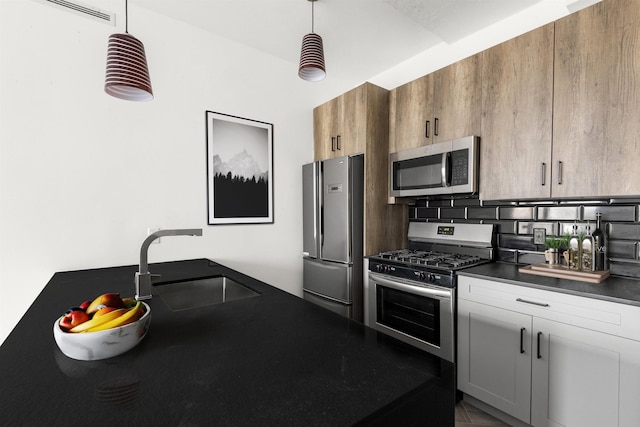 kitchen with a sink, hanging light fixtures, appliances with stainless steel finishes, backsplash, and dark countertops