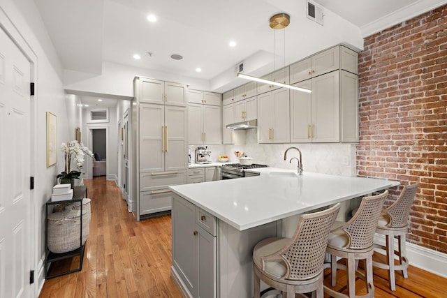 kitchen featuring a peninsula, gray cabinets, stainless steel gas range, and a sink