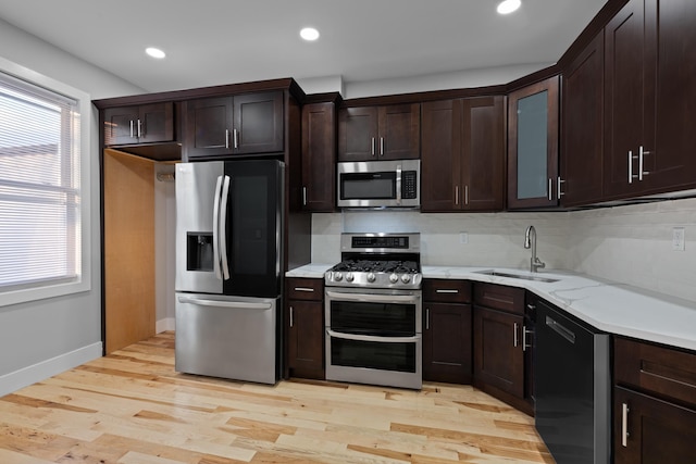 kitchen featuring stainless steel appliances, dark brown cabinets, sink, light hardwood / wood-style flooring, and tasteful backsplash