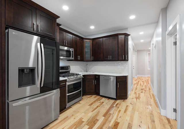 kitchen featuring stainless steel appliances, light hardwood / wood-style floors, decorative backsplash, dark brown cabinetry, and sink