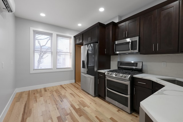 kitchen featuring appliances with stainless steel finishes, a wall mounted AC, light hardwood / wood-style floors, light stone counters, and decorative backsplash