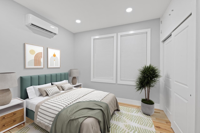 bedroom with a wall mounted AC and light hardwood / wood-style flooring