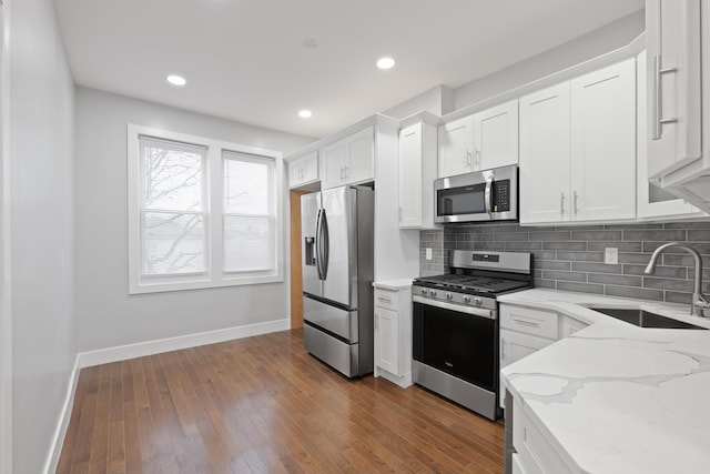 kitchen featuring stainless steel appliances, light stone countertops, sink, white cabinetry, and tasteful backsplash