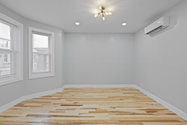 unfurnished room featuring an AC wall unit, light hardwood / wood-style floors, and a chandelier