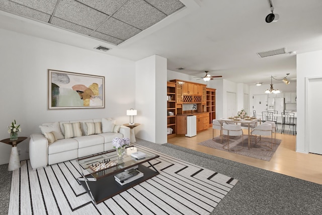 living area featuring ceiling fan with notable chandelier, visible vents, and wood finished floors