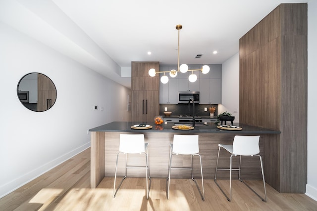 kitchen featuring a kitchen breakfast bar, hanging light fixtures, decorative backsplash, light wood-type flooring, and kitchen peninsula