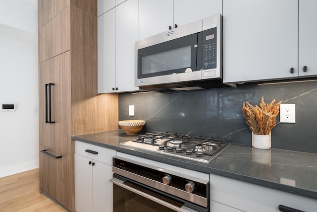 kitchen featuring white cabinets, decorative backsplash, light wood-type flooring, and stainless steel appliances