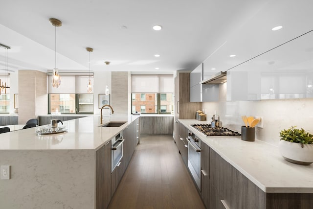 kitchen with light stone countertops, pendant lighting, stainless steel appliances, sink, and a large island