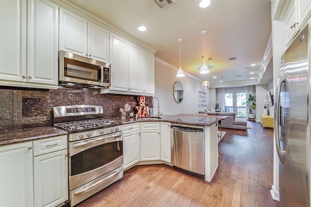 kitchen featuring pendant lighting, appliances with stainless steel finishes, ornamental molding, white cabinets, and kitchen peninsula