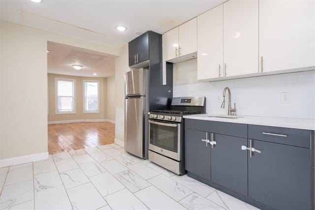 kitchen featuring light countertops, stainless steel appliances, marble finish floor, white cabinetry, and a sink