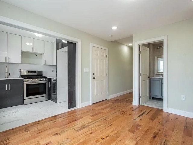 kitchen featuring light countertops, light wood-style floors, stainless steel gas stove, and baseboards