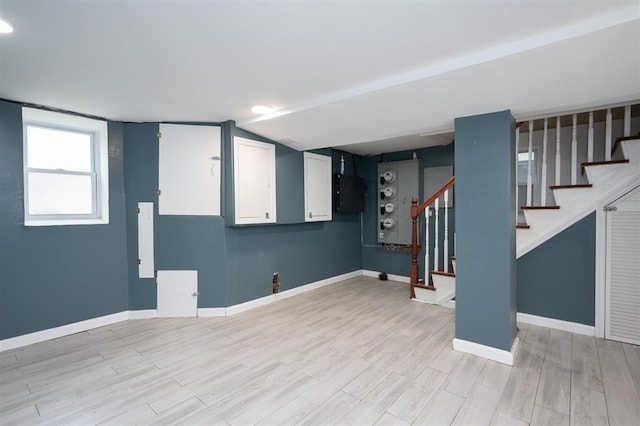 below grade area with baseboards, light wood-style floors, and stairs