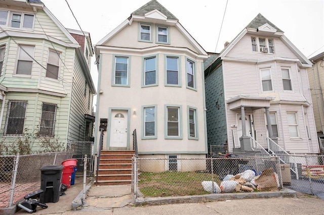 victorian house featuring entry steps, a fenced front yard, and stucco siding