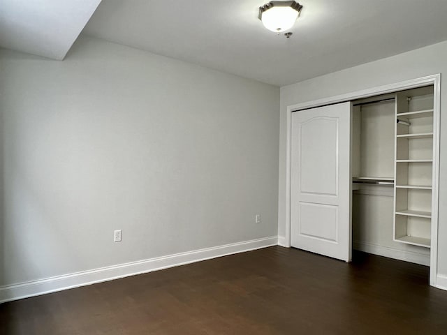 unfurnished bedroom with dark wood-type flooring, a closet, and baseboards