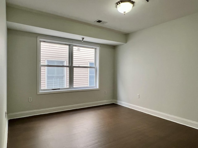 empty room featuring visible vents, dark wood finished floors, and baseboards