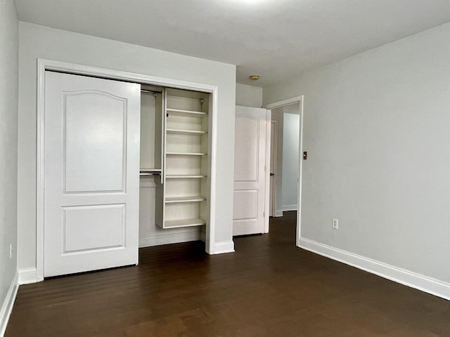 unfurnished bedroom featuring a closet, dark wood finished floors, and baseboards