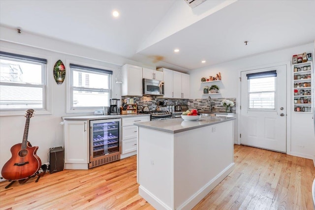 kitchen with a kitchen island, appliances with stainless steel finishes, white cabinets, beverage cooler, and light hardwood / wood-style flooring