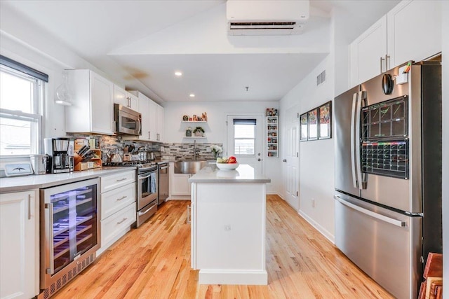 kitchen featuring appliances with stainless steel finishes, wine cooler, white cabinets, a kitchen island, and an AC wall unit