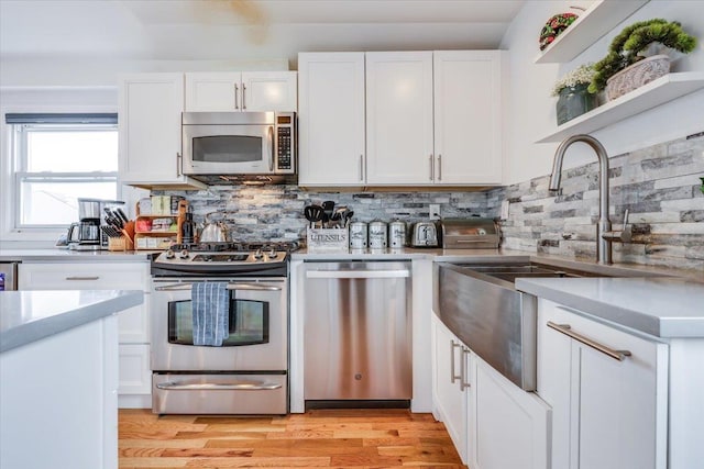 kitchen with tasteful backsplash, white cabinetry, sink, light hardwood / wood-style floors, and stainless steel appliances