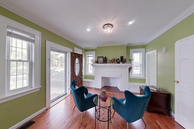 living area featuring light wood-type flooring, a wealth of natural light, ornamental molding, and a fireplace