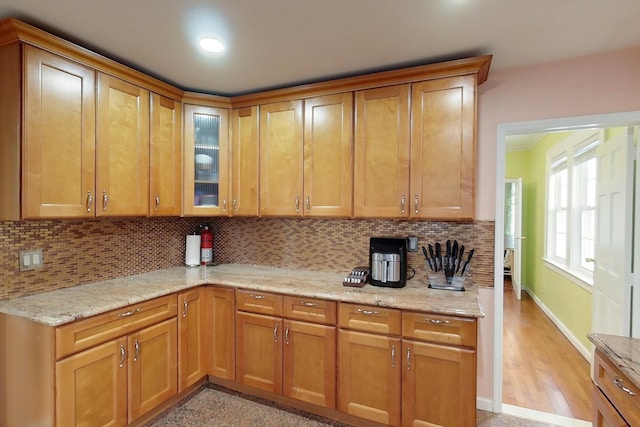 kitchen with light wood-type flooring, backsplash, and light stone counters