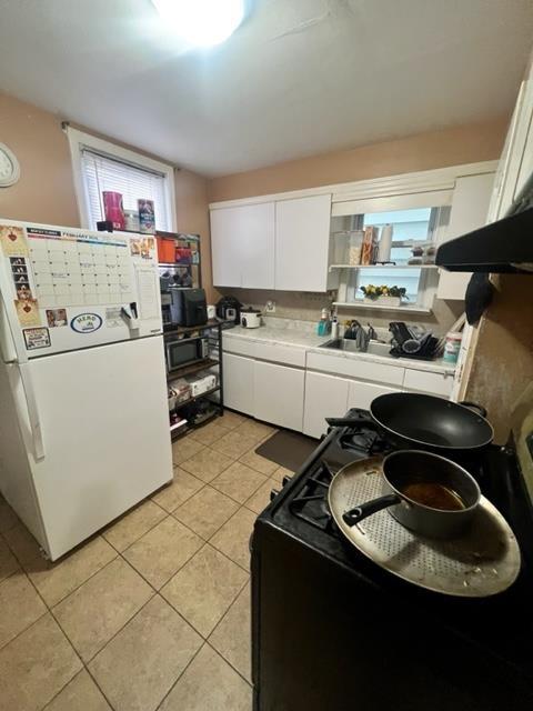 kitchen with light tile patterned flooring, black gas range, white cabinetry, light countertops, and freestanding refrigerator