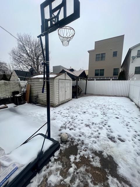 yard layered in snow featuring an outbuilding, a fenced backyard, and a storage shed