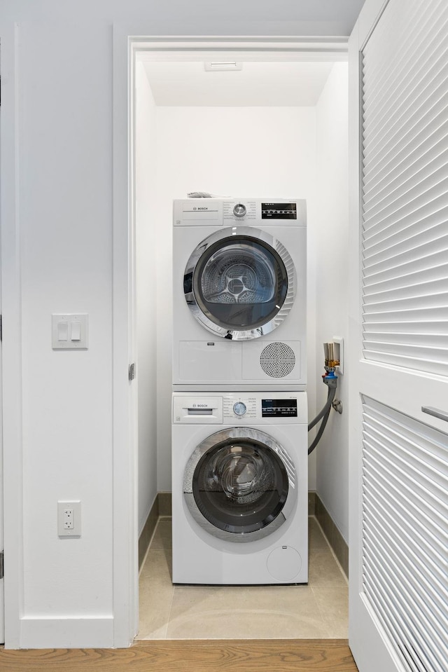 laundry area with stacked washer and dryer and light tile patterned floors