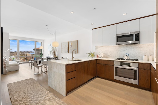 kitchen with light hardwood / wood-style floors, sink, kitchen peninsula, appliances with stainless steel finishes, and white cabinets