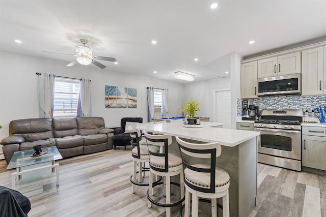 kitchen with appliances with stainless steel finishes, light hardwood / wood-style flooring, a kitchen island, and a breakfast bar area