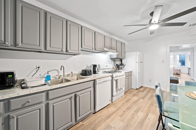 kitchen featuring light wood-type flooring, gray cabinets, white appliances, and a sink