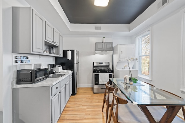 kitchen with stainless steel gas stove, visible vents, light wood-style floors, stacked washer / drying machine, and under cabinet range hood