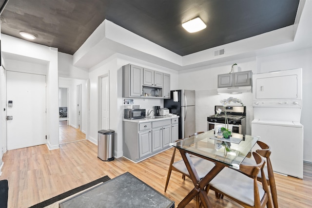 kitchen featuring stacked washer and clothes dryer, stainless steel appliances, gray cabinets, visible vents, and under cabinet range hood