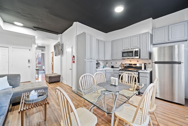 kitchen featuring light wood finished floors, stainless steel appliances, light countertops, and gray cabinetry