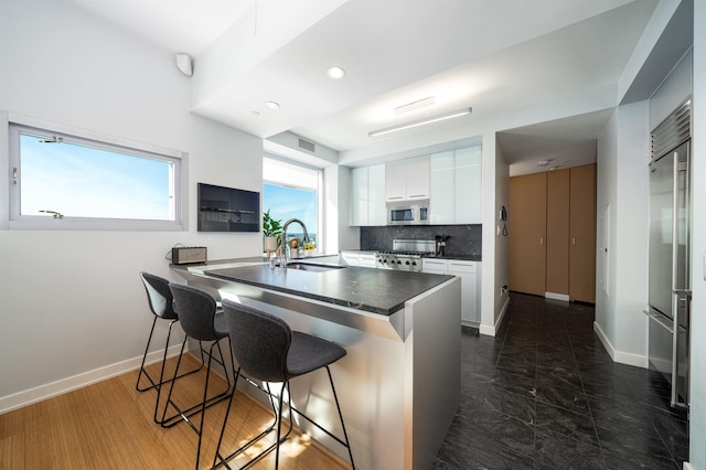 kitchen featuring white cabinetry, sink, stainless steel appliances, a kitchen breakfast bar, and decorative backsplash