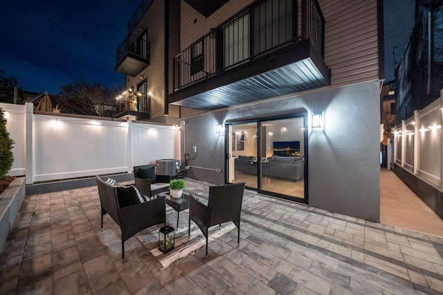 patio at night with an outdoor living space, a balcony, and central AC unit