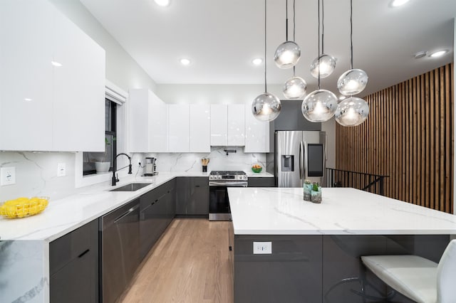 kitchen with appliances with stainless steel finishes, a kitchen island, sink, white cabinetry, and hanging light fixtures