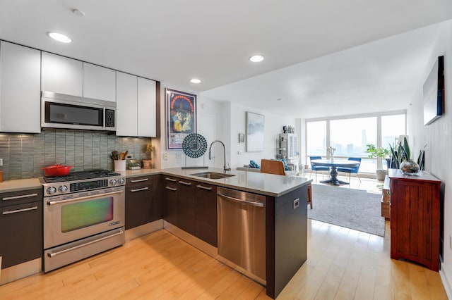 kitchen featuring decorative backsplash, appliances with stainless steel finishes, open floor plan, a peninsula, and a sink