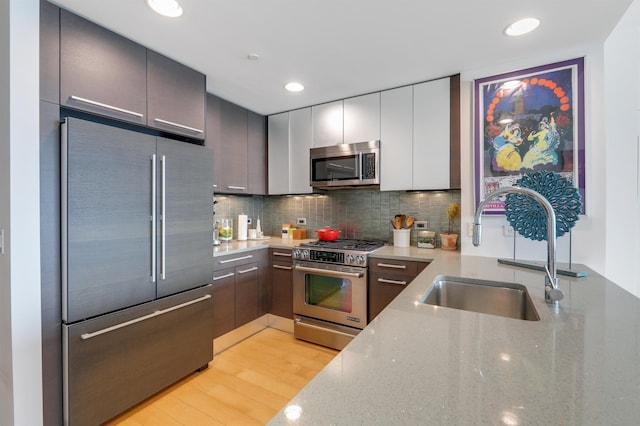 kitchen with light stone counters, stainless steel appliances, tasteful backsplash, light wood-style flooring, and a sink