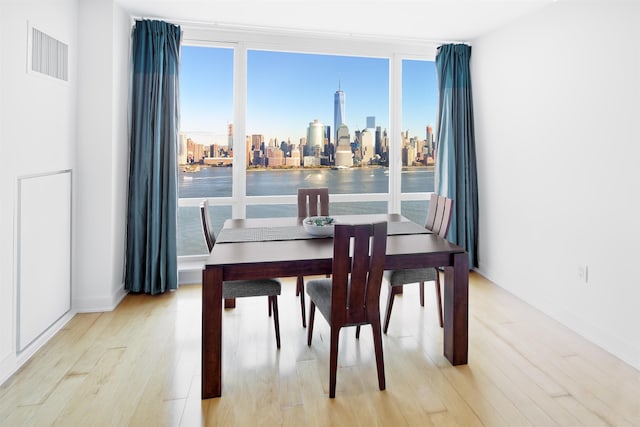 dining room with light wood-type flooring, a view of city, visible vents, and baseboards