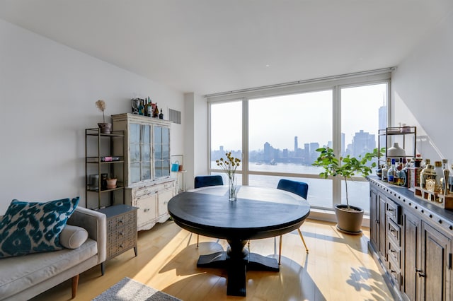 dining room with floor to ceiling windows, a city view, and light wood-style flooring