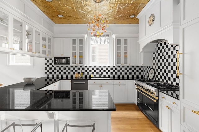 kitchen featuring a breakfast bar, decorative light fixtures, black microwave, dark stone counters, and double oven range