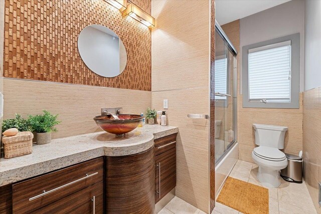 full bathroom with vanity, enclosed tub / shower combo, tile patterned flooring, tile walls, and toilet