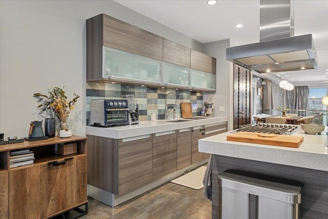 kitchen with a sink, glass insert cabinets, island range hood, light countertops, and decorative backsplash