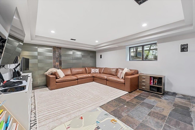 living room featuring recessed lighting, a tray ceiling, and stone tile floors