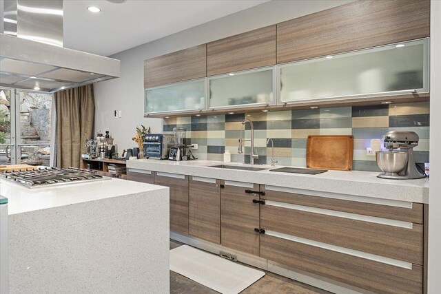 kitchen with tasteful backsplash, stainless steel gas cooktop, light countertops, island range hood, and a sink